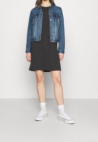 Jeansjacka med klassisk skärning, mörkgrå klänning och vita hög-top sneakers. Enkelt design med en avslappnad, lager-på-lager-look.