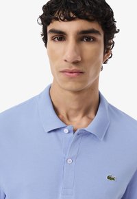 Polo shirt azzurro chiaro in cotone, con colletto a coste, pattina con tre bottoni e logo del coccodrillo ricamato sul lato sinistro del petto.