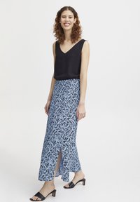 Zwarte mouwloze top; blauwe maxi rok met zwart bloemenkantpatroon; zijsplit; model draagt zwarte hoge sandaaltjes.
