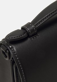 Bolso de cuero negro con una textura suave, que presenta una solapa redondeada, acentos cosidos y un detalle de correa asegurada en el lado.