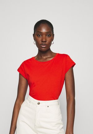 Red short-sleeved t-shirt, round neckline, soft cotton material, paired with high-waisted white trousers and a silver button detail.