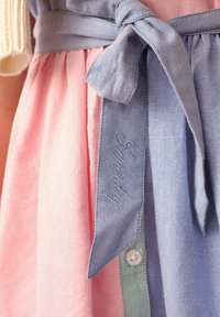Tweedekleurige jurk met een roze rok en een blauwe denim tailleband. De riem is geknoopt en toont geborduurde branding en een knoopdetail.