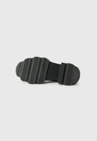 Black rubber shoe sole with a textured surface, featuring prominent ridges and a rounded toe. No visible branding on the sole.