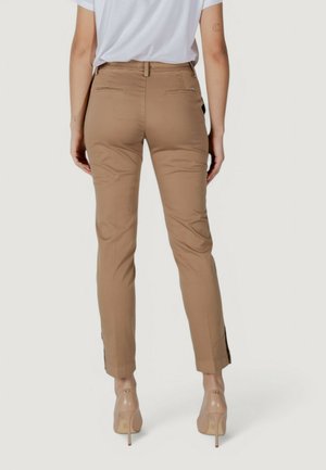 Pantalones ajustados de color beige con bolsillos traseros y aberturas laterales en el dobladillo. Combinados con una camisa blanca y tacones transparentes. Textura de tela suave.