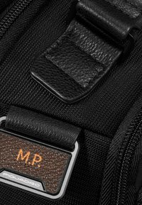 Tessuto nero con una fibbia in pelle nera testurizzata e una targhetta metallica rettangolare con la scritta "M.P." in arancione. Dettagli in metallo argentato.