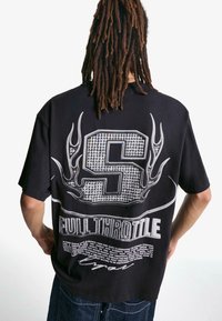Črna oversized majica z diamanti oblikovano črko "S" z rogovnimi motivi ter napisom "FULL THROTTLE" na hrbtu, iz bombažnega materiala.