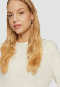 Lichte, gebreide trui in zacht Roomwit met een textuurpatroon. Heeft een ronde hals en lange mouwen, gedragen met steil blond haar.