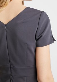 Grau Kleid mit kurzen Ärmeln, V-Ausschnitt, strukturiertem Stoff mit dezenten Mustern und einem sichtbaren Reißverschluss im Rücken.