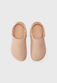 Sabots slip-on couleur pêche en tissu texturé, avec des orteils ronds et des sangles à l'arrière. Design minimaliste avec des bords lisses et des semelles plates.