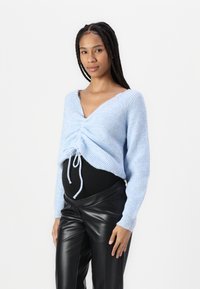 Lichtblauwe gebreide trui met een diepe halslijn, geraffineerde voorkant en koorddetail, gecombineerd met zwarte, hoogzwaaiende nep leren broek.