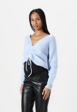 Light blue knitted sweater with a plunging neckline, gathered front, and drawstring detail, paired with black, high-waisted faux leather pants.