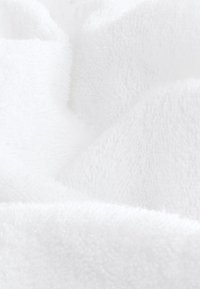 Tissu éponge blanc doux avec boucles visibles et texture, plié et superposé en courbes douces.
