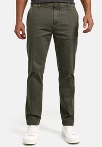 Pantalones de algodón verde oliva con un diseño de pierna recta, que cuentan con bolsillos frontales, cierre de botón y puños en el dobladillo, combinados con zapatillas blancas.
