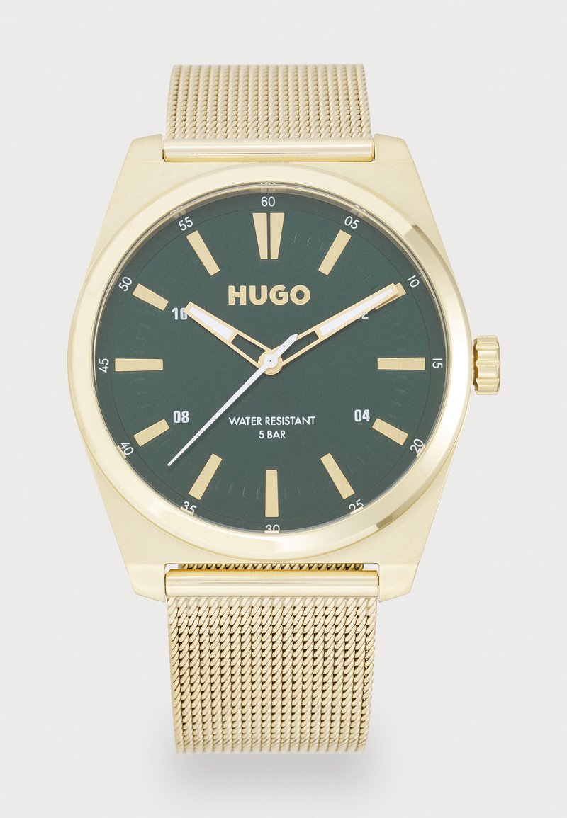 Reloj dorado con esfera verde, que presenta marcadores de hora dorados, manecillas blancas y una pulsera de malla. Resistente al agua hasta 5 bares.