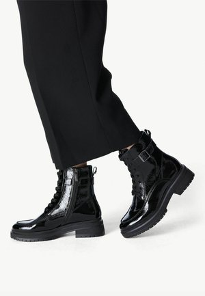 Black patent leather ankle boots with a chunky sole, lace-up front, and side zipper. Features a buckle detail on the ankle.