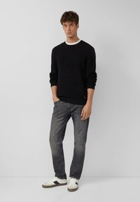 Czarny sweter z dzianiny o prążkowanej fakturze, w połączeniu z szarymi dżinsami. Białe i czarne sneakersy o minimalistycznym designie.