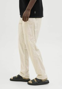 Béžové kalhoty s širokými nohavicemi z lehké látky, doplněné černými nazouvacími sandály s nastavitelnými pásky a polstrovanou podrážkou.