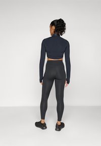 Zwarte crop top met lange mouwen, textuur aan de achterkant, gecombineerd met hoge zwarte leggings en zwarte sportschoenen. Glad, aansluitend ontwerp.