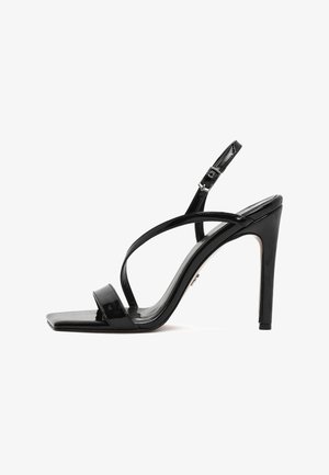 Sandalia de tacón alto de charol negro con punta cuadrada, finas tiras entrecruzadas, correa ajustable en el tobillo y tacón de aguja.