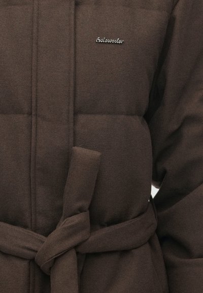 Brun polstret jakke med et bundet bælte, der har et subtilt logo. Stoffet har en struktureret overflade og synlig quiltet mønster.