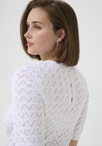 Maglione bianco lavorato a maglia con un motivo geometrico, dotato di maniche corte e chiusura con bottone sul retro con dettagli in perle.