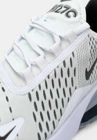 Nike tekaški čevlj z večinoma belim mrežnim zgornjim delom, ki ima sivo perforacijo, bele vezalke in črn logotip na strani.