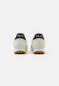Adidași din suede alb și gri cu tab-uri negre la călcâi care prezintă logo-ul "VEJA". Talpă din cauciuc cu model de tracțiune. Design minimalist.