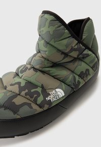 Både slippers med camouflage-mønster fra The North Face, laget av quiltet grønn og svart syntetisk materiale, med avrundet form og gummisåle.