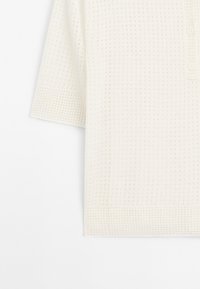 Korte mouwen, wit gebreid topje met een gestructureerd, patroonoppervlak en een drie-knopen sluiting bij de kraag, met een relaxte pasvorm.