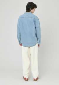 Chemise en denim bleu clair avec un col boutonné, des manches longues et un ourlet arrondi. Associée à un pantalon crème et des sandales rouges à motifs.