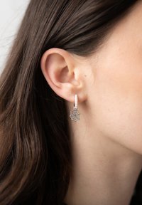 Orecchino a cerchio in argento con superficie texturizzata, caratterizzato da un ciondolo a forma di ragnatela. Piccole perle accentuano il design complessivo.