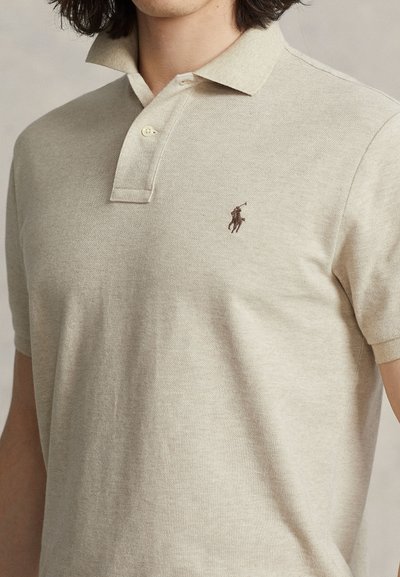 Béžové polokošeľa z textúrovaného materiálu, s dvojgombíkovým zapínaním a golierom. Na hrudi má malé hnedé vyšívané logo.