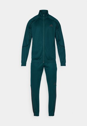 Survêtement en bleu sarcelle avec une veste zippée et un pantalon fuselé assorti. Comprend des accents noirs et un logo sur la poitrine et la jambe. Tissu lisse.