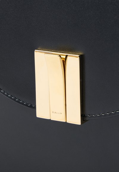 Black leather bag featuring a prominent gold-toned clasp with two curved sections. Subtle stitching detailing and embossed brand name visible.