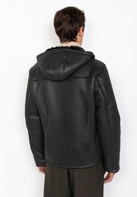 Schwarze Lederjacke mit Kapuze, die eine glatte Textur und ein schlichtes Design aufweist. Die Rückseite zeigt Nähdetails und eine taillierte Form.