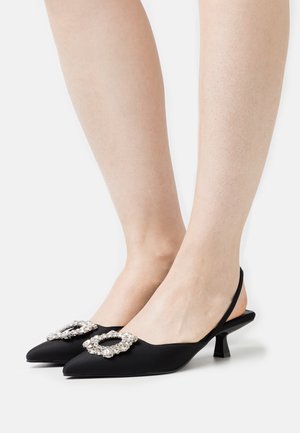 Des escarpins noir à talons kitten avec bride arrière, chaque chaussure ornée d'une grande boucle en cristal rond sur le dessus.