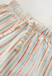 Črtaste kratke hlače v krem barvi z modrimi in rdečimi navpičnimi črtami. Elastičen pas s trakom za nastavljivo prileganje. Mehka, teksturirana tkanina.