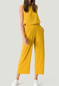 Ensemble en deux pièces texturé jaune comprenant un haut sans manches et un pantalon à jambes larges, associé à des baskets blanches. Design simple, coupe décontractée.