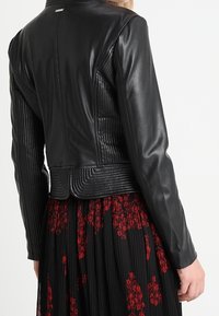 Czarna skórzana kurtka z prążkowaną fakturą na plecach i ramionach, z dopasowanym krojem i lekko podniesionym kołnierzem.