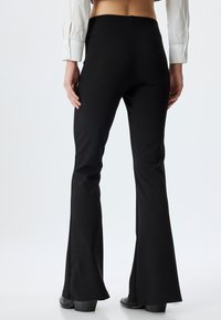Pantalones de campana negros hechos de material elástico con una textura suave. Ajustados en la cintura y las caderas, se ensanchan por debajo de la rodilla.