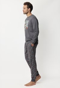Top gris de manga larga con diseño gráfico, combinado con pantalones grises que tienen patrones de hojas coloridos. Ambos están hechos de una tela suave y tienen un corte relajado.