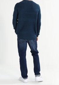 Dunkelblauer Rippstrickpullover mit Rundhalsausschnitt, kombiniert mit geraden, dunklen Jeans und weißen Sneakers.