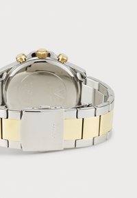 Silver and gold two-tone metal watch band with a clasp; features three gold pushers and a polished dial with circular case and engraved back.