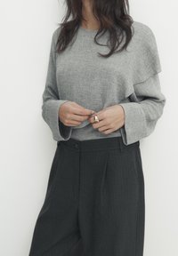 Grijze, textuur langs mouwen top met een gelaagd ontwerp, gecombineerd met hoog uitgesneden, donkergrijze pinstripe broek met voorplooien en knopen.