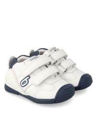 Zapatos de cuero blancos con detalles en azul marino, que cuentan con dos tiras de Velcro, forma redondeada, suelas de goma y un pequeño logotipo en el costado.