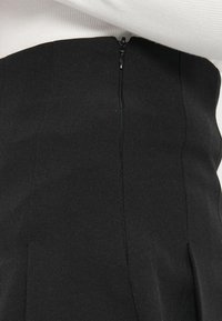 Μαύρο παντελόνι με ψηλή μέση και λεία υφασμάτινη επιφάνεια. Διαθέτει κρυφό φερμουάρ στο πίσω μέρος και κάθετες ραφές για εφαρμογή που αγκαλιάζει το σώμα.