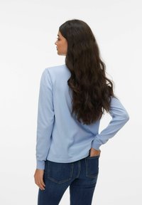 Pull-over bleu clair à manches longues avec une texture lisse, col rond et poignets côtelés, associé à un jean bleu foncé.