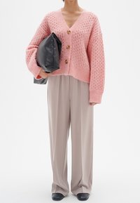Pink knitted cardigan with a V-neck, three button closure, and loose fit. Paired with light beige wide-leg trousers and black shoes.