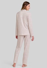 Conjunto de pijama con estampado floral en tejido suave y ligero; incluye una camisa de manga larga con cuello y pantalones a juego. Colores en rosa pálido y crema.