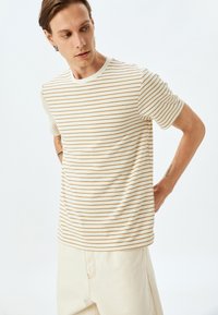 Camiseta de manga corta a rayas en crema y beige, con un escote redondo y un corte relajado. Tejido suave con finas líneas horizontales.
